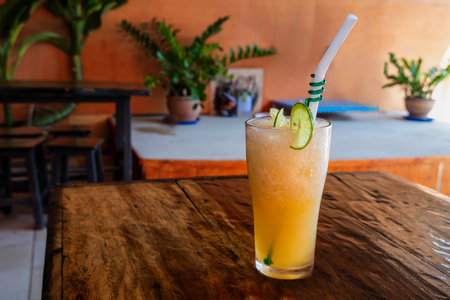 Orange juice in glass closed cup with tube on wooden table and yellow wall backgroundの写真素材