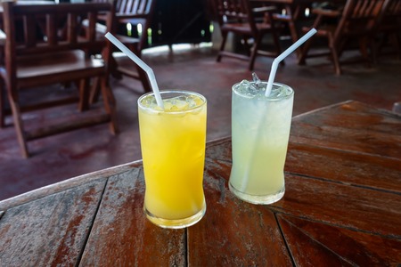 Two glass of fresh fruit juices on the wooden table. Orange and lemon  juices on table in cafeの写真素材