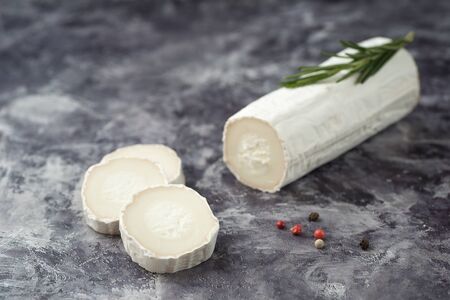 Delicious goat cheese slices and piece with fresh rosemary leaves on stone  background. Luxurious culinary cheese still life.の写真素材