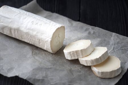 Delicious goat cheese slices and piece with red berries  on black wooden background. Luxurious culinary cheese still life.の写真素材