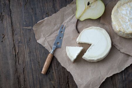 Brie type of cheese. Camembert cheese. Fresh Brie cheese and a slice on a wooden board with pear and knife. Italian, French cheese.の写真素材