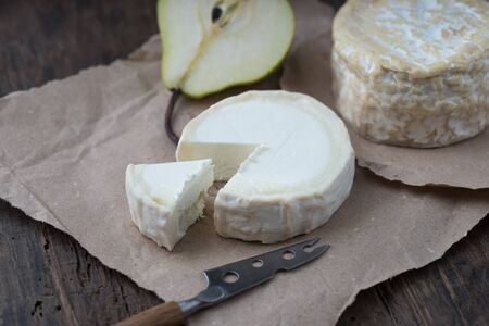 Brie type of cheese. Camembert cheese. Fresh Brie cheese and a slice on a wooden board with pear and knife. Italian, French cheese.の写真素材