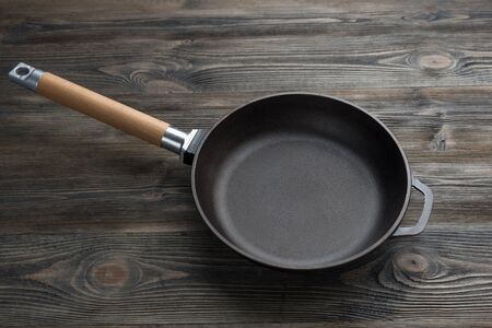 Empty cast iron frying pan on wooden culinary background.の写真素材