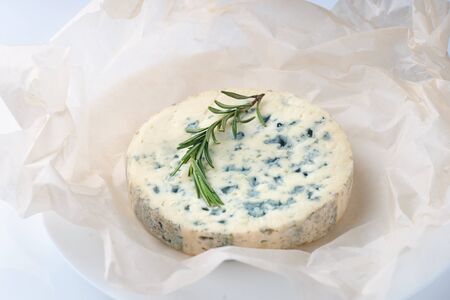 Blue cheese with sprigs of rosemary on sheets of paper and white table backgroundの写真素材