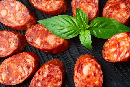 A lot of pieces of dried sausage on a dark wood background. Minimalistic composition of food.  Ingredient from meatの写真素材