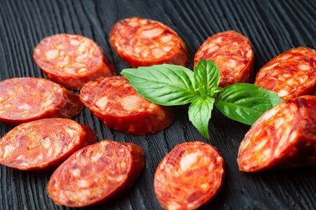 A lot of pieces of dried sausage on a dark wood background. Minimalistic composition of food.  Ingredient from meatの写真素材