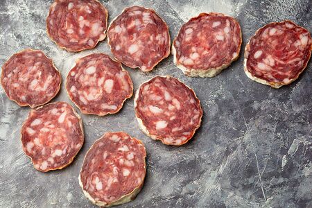 A lot of pieces of dried sausage on a dark stone background. Minimalistic composition of food.