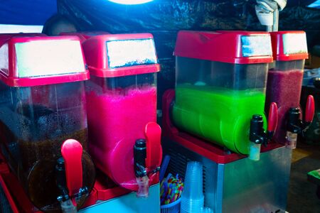 Four different color slush drink containers in a row, outdoors in summer.の写真素材