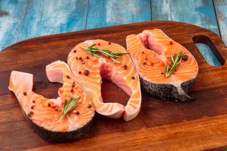 A three pieces of raw salmon, spices, board, salt rosemary on the old shabby blue table, top view. Preparation for cooking fish food. Salmon steak.の写真素材