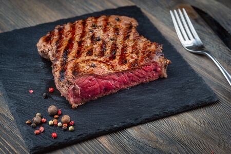 Sliced medium rare grilled Beef steak Ribeye with roasted on black stone board on wooden backgroundの写真素材