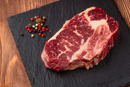 Fresh raw Prime Black Angus beef steaks on stone board: Striploin, Rib Eye. Top view. On a dark wood backgroundの写真素材