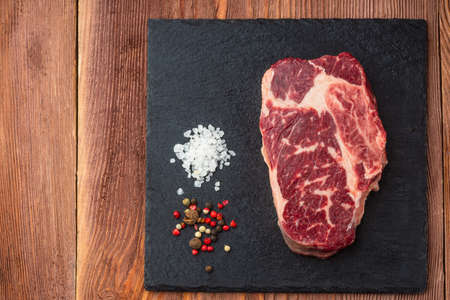 Fresh raw Prime Black Angus beef steaks on stone board: Striploin, Rib Eye. Top view. On a dark wood backgroundの写真素材