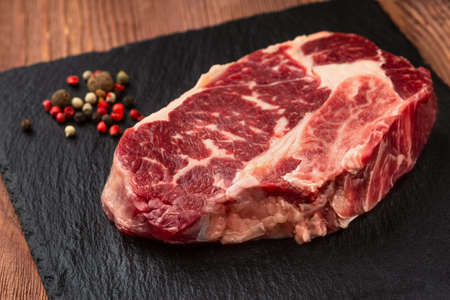 Fresh raw Prime Black Angus beef steaks on stone board: Striploin, Rib Eye. Top view. On a dark wood backgroundの写真素材