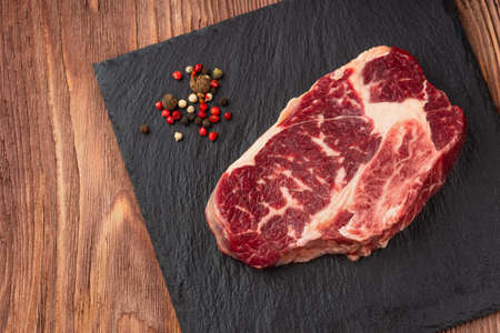 Fresh raw Prime Black Angus beef steaks on stone board: Striploin, Rib Eye. Top view. On a dark wood backgroundの写真素材