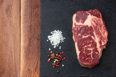 Fresh raw Prime Black Angus beef steaks on stone board: Striploin, Rib Eye. Top view. On a dark wood backgroundの写真素材
