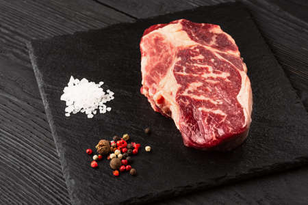 Fresh raw Prime Black Angus beef steaks on stone board: Striploin, Rib Eye. Top view. On a dark backgroundの写真素材