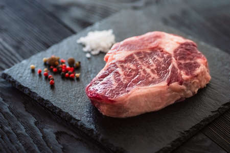 Fresh raw Prime Black Angus beef steaks on stone board: Striploin, Rib Eye. Top view. On a dark backgroundの写真素材