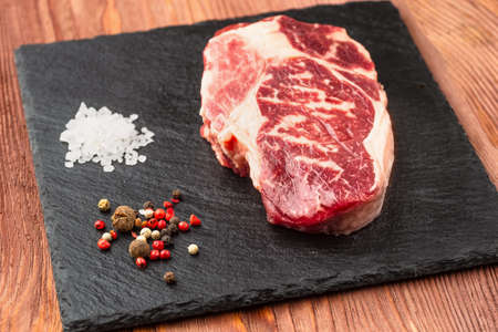 Fresh raw Prime Black Angus beef steaks on stone board: Striploin, Rib Eye. Top view. On a dark backgroundの写真素材