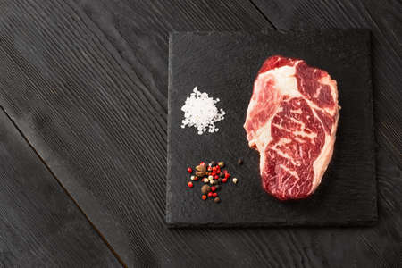 Fresh raw Prime Black Angus beef steaks on stone board: Striploin, Rib Eye. Top view. On a dark backgroundの写真素材