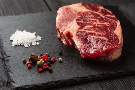 Fresh raw Prime Black Angus beef steaks on stone board: Striploin, Rib Eye. Top view. On a dark backgroundの写真素材
