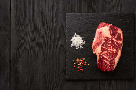 Fresh raw Prime Black Angus beef steaks on stone board: Striploin, Rib Eye. Top view. On a dark backgroundの写真素材