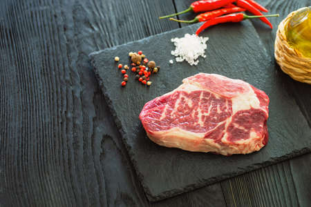 Fresh raw Prime Black Angus beef steaks on stone board: Striploin, Rib Eye. Top view. On a dark backgroundの写真素材