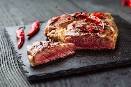 Sliced medium rare grilled steak on rustic stone board with chili and spices , dark rustic wooden background, top view, place for textの写真素材