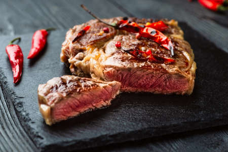 Sliced medium rare grilled steak on rustic stone board with chili and spices , dark rustic wooden background, top view, place for textの写真素材