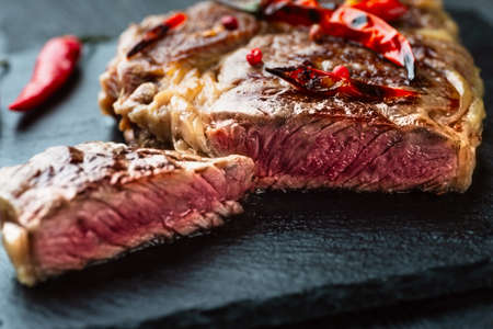 Sliced medium rare grilled steak on rustic stone board with chili and spices , dark rustic wooden background, top view, place for textの写真素材