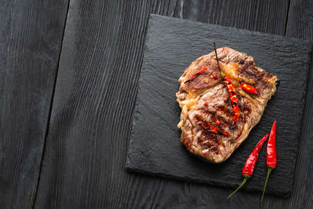 Sliced medium rare grilled steak on rustic stone board with chili and spices , dark rustic wooden background, top view, place for textの写真素材