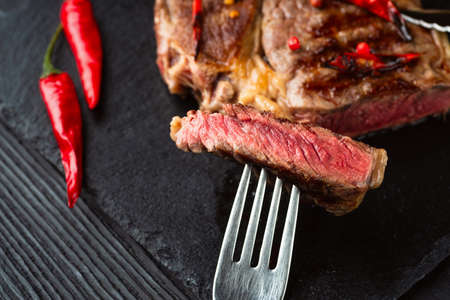 Sliced medium rare grilled steak on rustic stone board with chili and spices , dark rustic wooden background, top view, place for textの写真素材