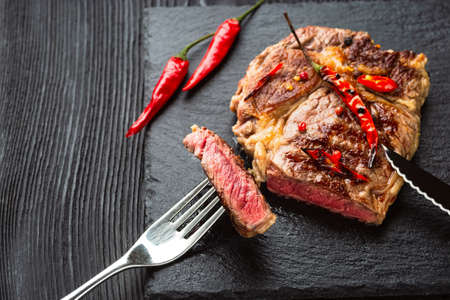 Sliced medium rare grilled steak on rustic stone board with chili and spices , dark rustic wooden background, top view, place for textの写真素材