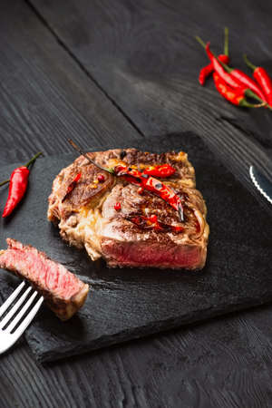 Sliced medium rare grilled steak on rustic stone board with chili and spices , dark rustic wooden background, top view, place for textの写真素材