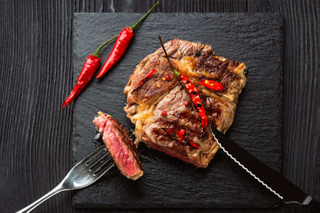 Sliced medium rare grilled steak on rustic stone board with chili and spices , dark rustic wooden background, top view, place for textの写真素材