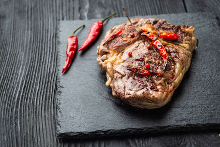 Sliced medium rare grilled steak on rustic stone board with chili and spices , dark rustic wooden background, top view, place for textの写真素材