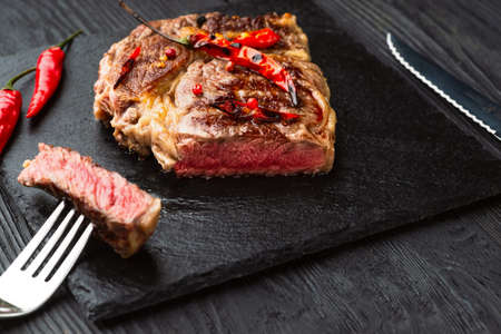 Sliced medium rare grilled steak on rustic stone board with chili and spices , dark rustic wooden background, top view, place for textの写真素材