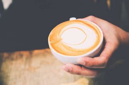 Closeup image of male barista holding and pouring milk for prepare cup of coffee, latte art, vintage color tone, coffee preparation and service concept, lifestyleの写真素材