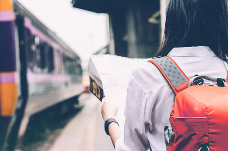 Girl wearing backpack holding map, waiting for a train. Traveling in Bangkok Thailand. Travel conceptの写真素材