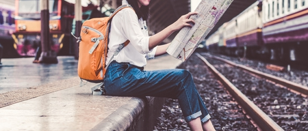 Girl wearing backpack holding map, waiting for a train. Traveling in Bangkok Thailand. Travel conceptの写真素材
