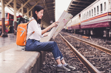 Girl wearing backpack holding map, waiting for a train. Traveling in Bangkok Thailand. Travel conceptの写真素材