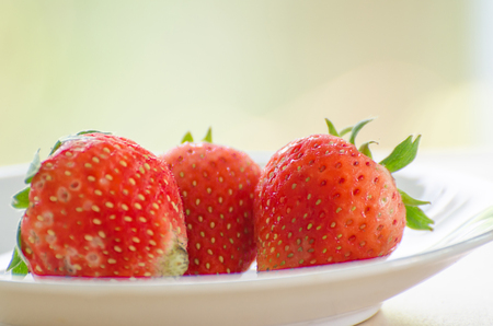 Ripe strawberries with leaves in wicker basket on wooden table on blurred backgroundの写真素材
