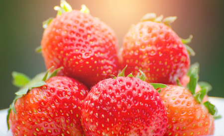 Ripe strawberries with leaves in wicker basket on wooden table on blurred backgroundの写真素材