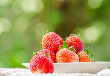 Ripe strawberries with leaves in wicker basket on wooden table on blurred backgroundの写真素材