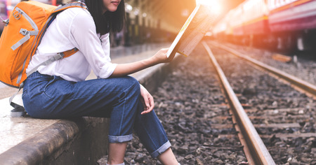 Girl wearing backpack holding map, waiting for a train. Traveling in Bangkok Thailand. Travel conceptの写真素材