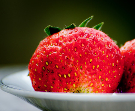 Ripe strawberries with leaves in wicker basket on wooden table on blurred backgroundの写真素材