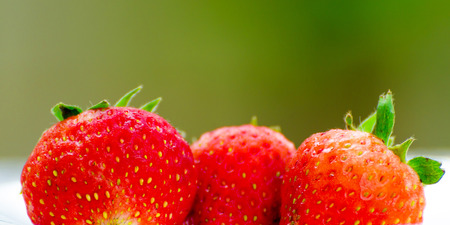 Ripe strawberries with leaves in wicker basket on wooden table on blurred backgroundの写真素材