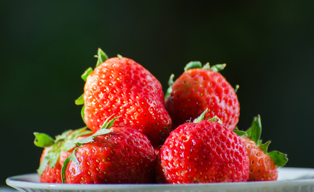 Ripe strawberries with leaves in wicker basket on wooden table on blurred backgroundの写真素材