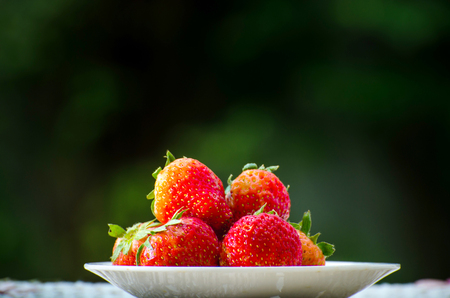 Ripe strawberries with leaves in wicker basket on wooden table on blurred backgroundの写真素材