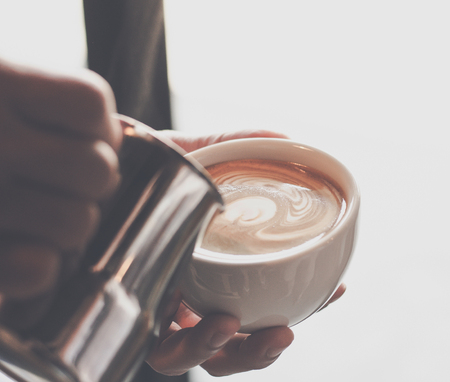 Closeup image of male barista holding and pouring milk for prepare cup of coffee, latte art, vintage color tone, coffee preparation and service concept, lifestyleの写真素材