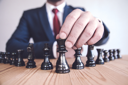 Retro style image of a businessman with clasped hands planning strategy with chess figures on an old wooden table.の写真素材